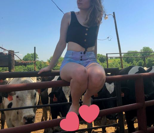 Eine junge Frau sitzt auf einem Gatter. Sie hat ihre Füße durch Herz-Emojis zensiert.